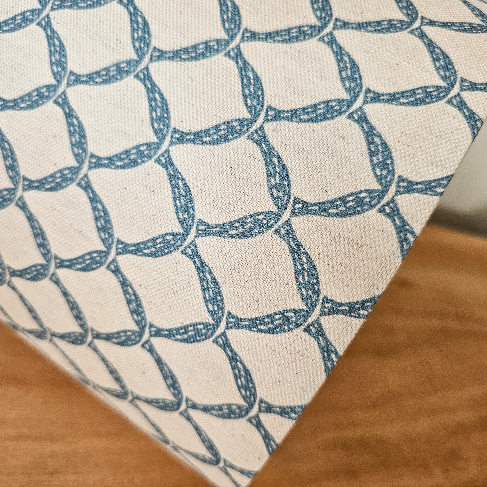 Marina cotton linen fabric featuring a repeating blue curved geometric trellis motif on an off‑white textured background.  Featured on a close up lampshade ZIA LIVING.