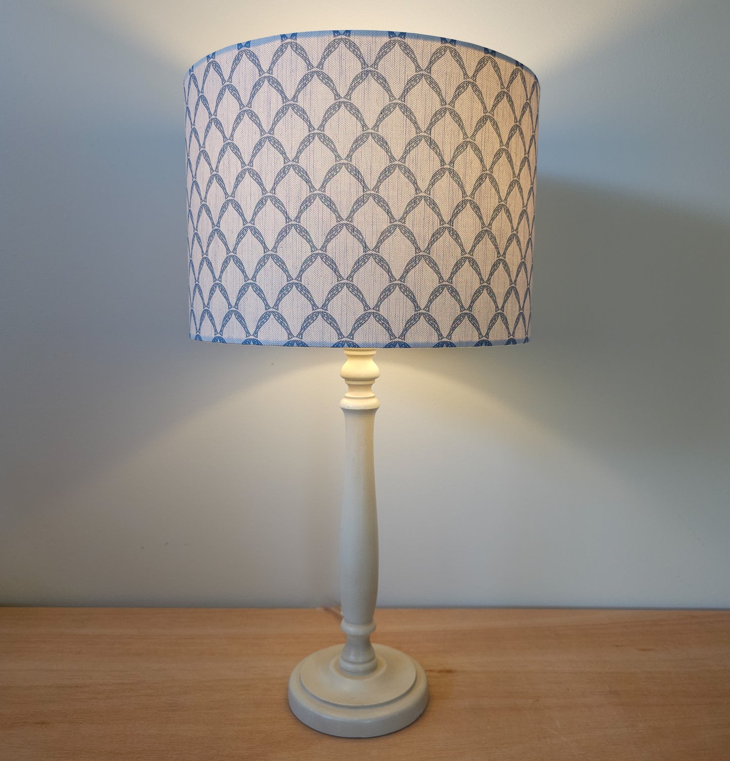 Marina cotton linen fabric featuring a repeating blue curved geometric trellis motif on an off‑white textured background. Featured on a lampshade and base. cosy setting ZIA LIVING.
