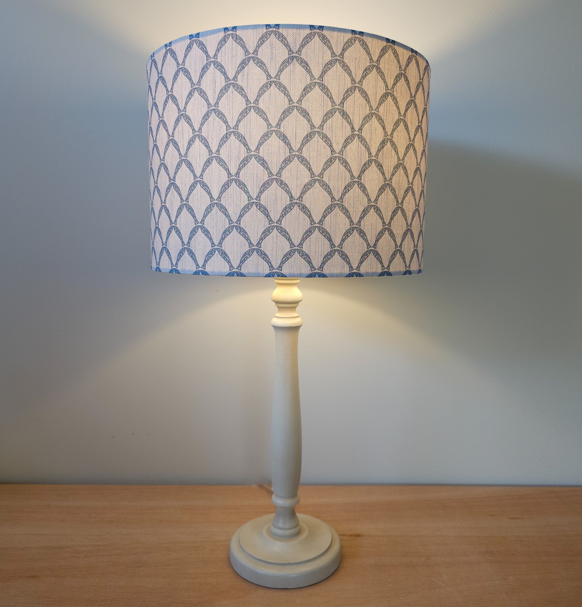 Marina cotton linen fabric featuring a repeating blue curved geometric trellis motif on an off‑white textured background. Featured on a lampshade and base. cosy setting ZIA LIVING.