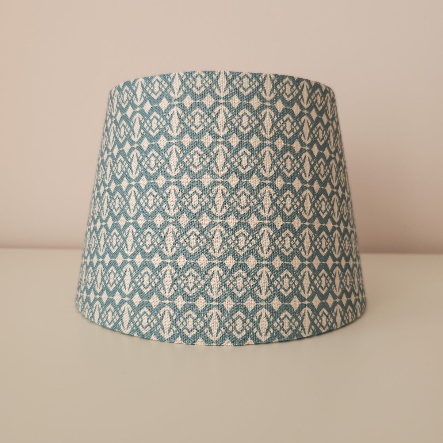 Fornet print wall light shade with a warm glow, featuring a soft geometric  pattern. front view— ZIA LIVING.