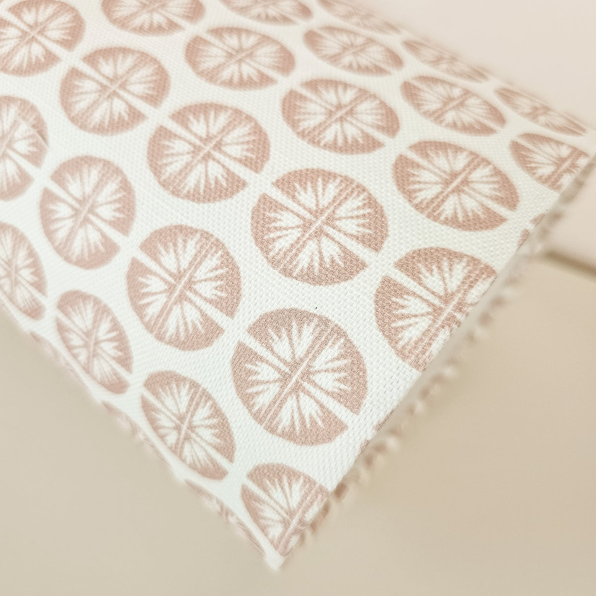 Close up of a drum shade featuring a repeating dusty rose circular pressed flower pattern on a white fabric background, set against a green panelled wall.