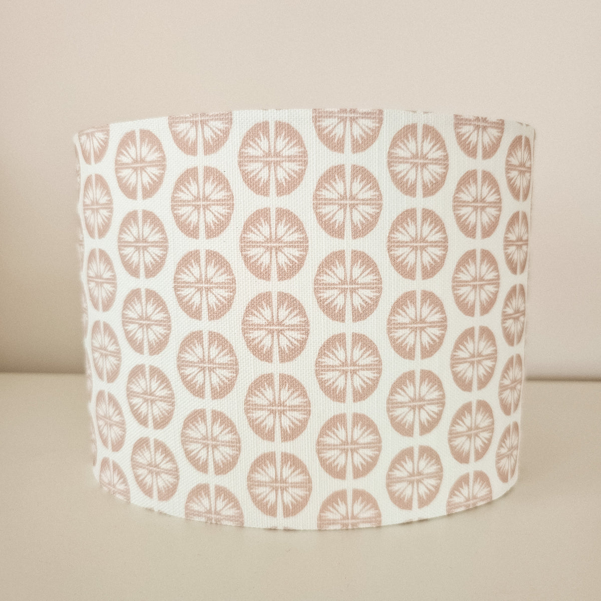 Dusty rose circular pressed flower pattern on a white fabric background lampshade front view on white surface. 