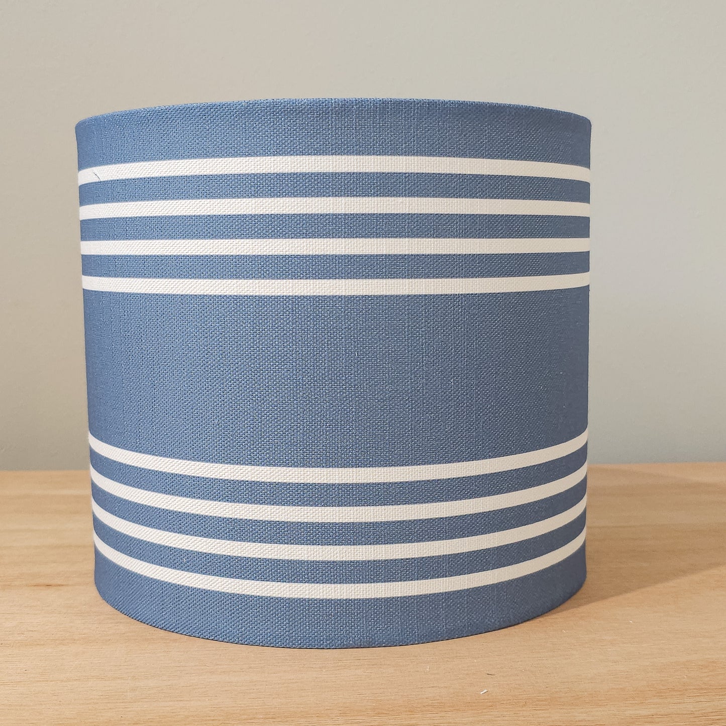 Drum lampshade in Blue Studio Stripe fabric with horizontal stripe pattern on wooden surface — artisan home décor by ZIA LIVING.