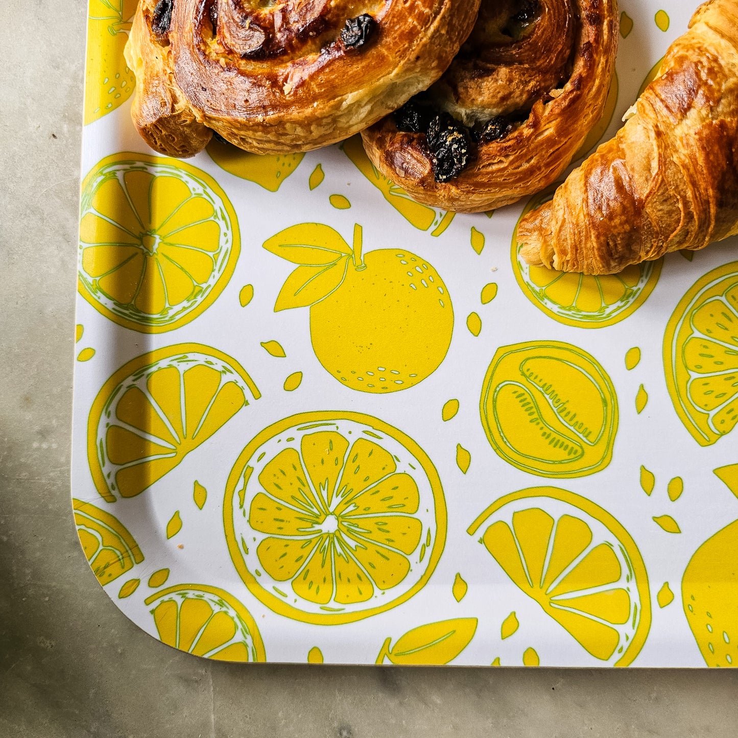 White rectangular tray with a bright yellow lemon and citrus slice pattern, styled on a marble surface, with pastries for a fresh, summery kitchen look. ZIA LIVING