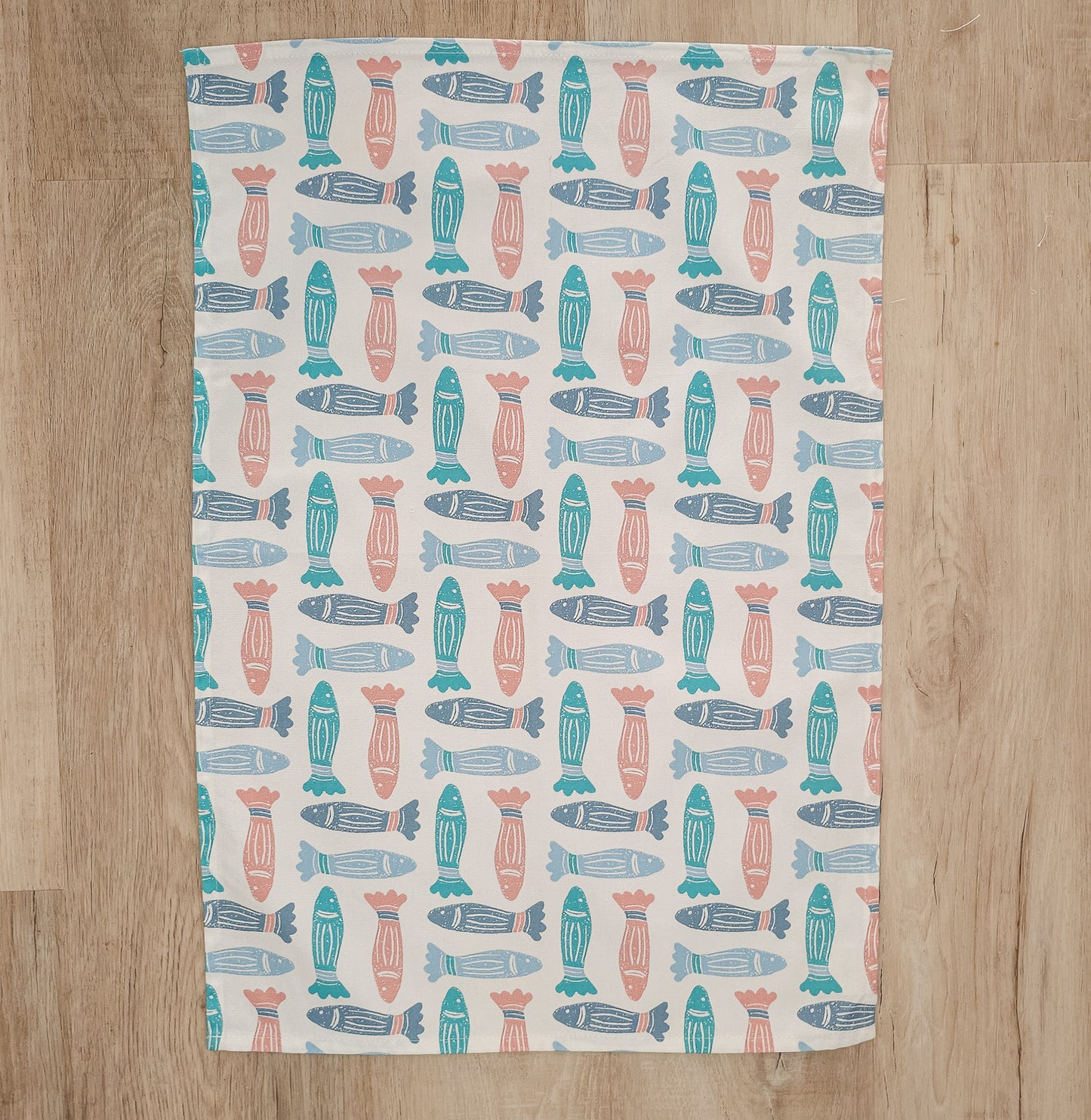 A colourful fish print designed tea towel from Zia-Living arranged flat showing full design on a wooden worktop 