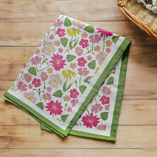 Floral sumer garden print tea towel from Zia Living with green border on a wooden surface