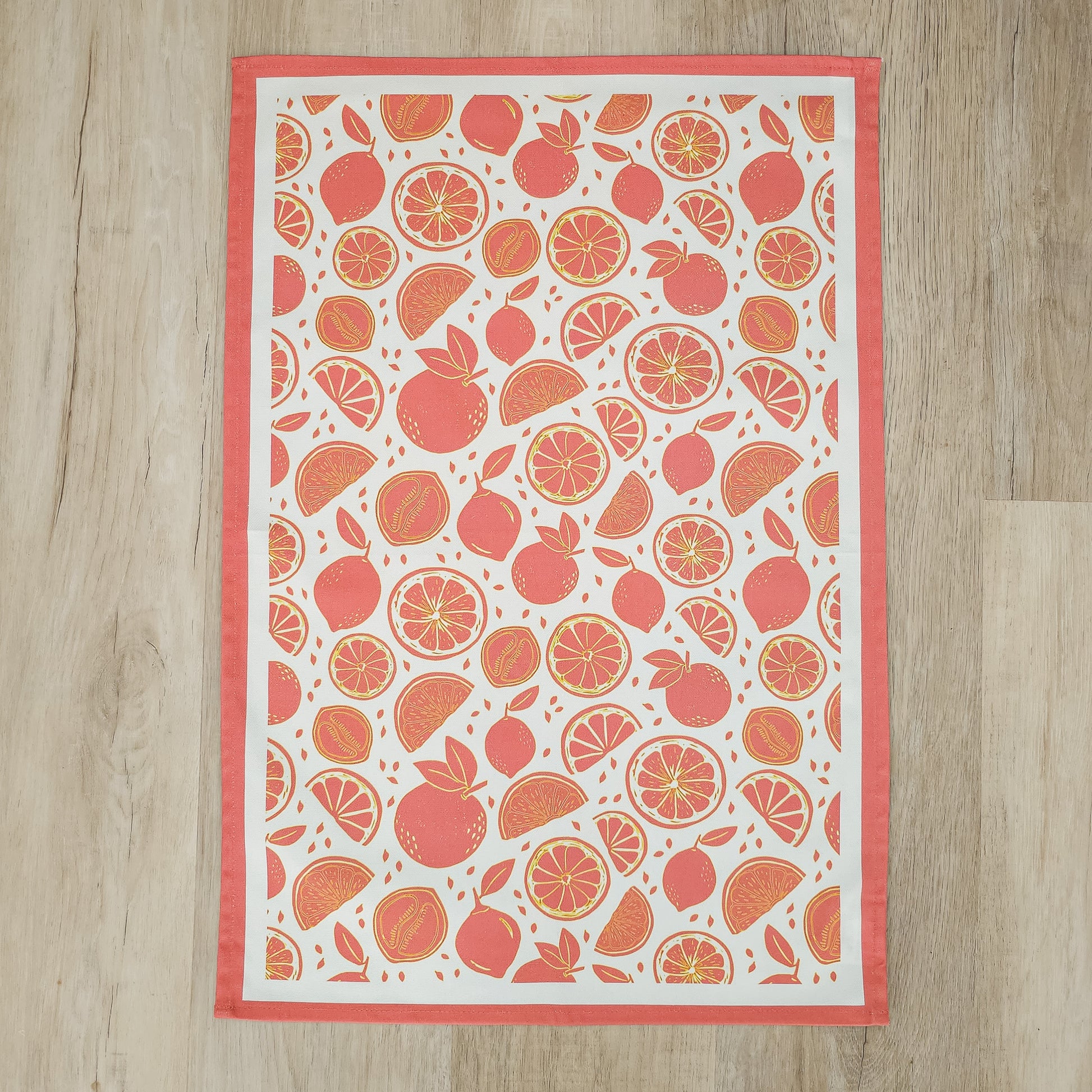 An orange‑and‑white citrus‑print tea towel from ZIA LIVING laid flat on a wooden worktop.
