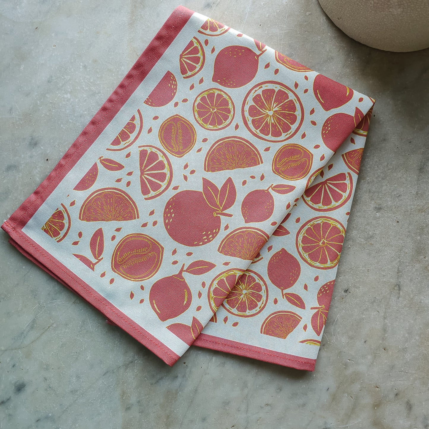 An orange‑and‑white citrus‑print tea towel from ZIA LIVING folded on a marble kitchen worktop