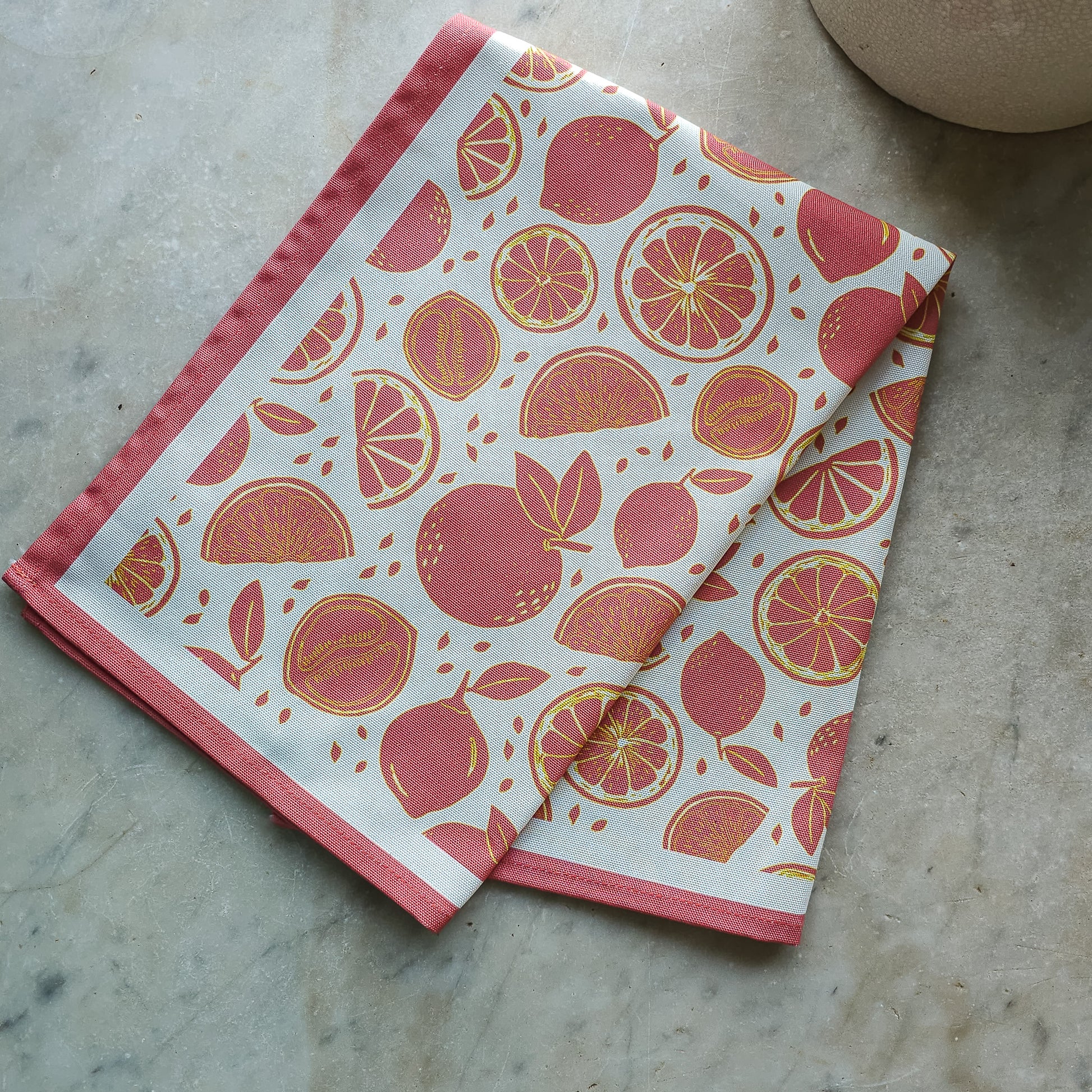 An orange‑and‑white citrus‑print tea towel from ZIA LIVING folded on a marble kitchen worktop