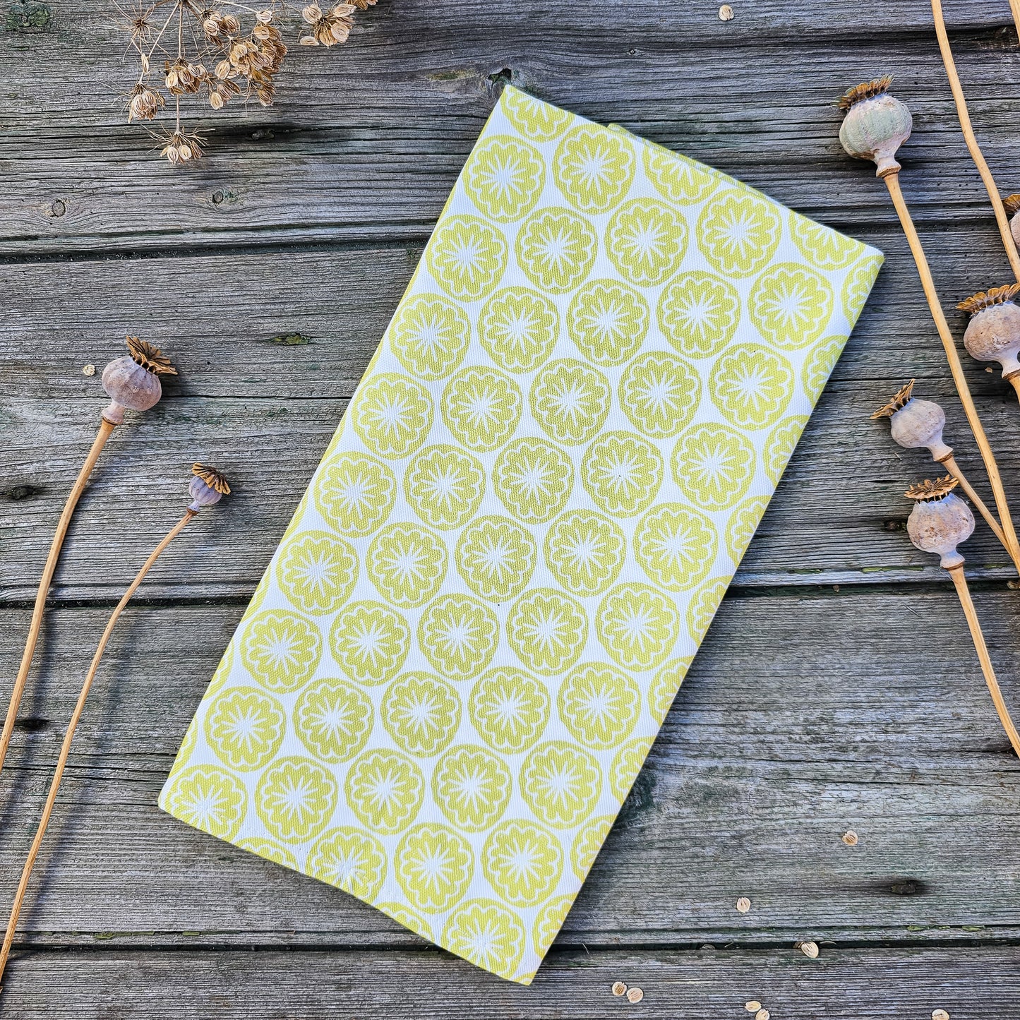Yellow Seedhead patterned fabric folded on a wooden surface, featuring bold circular  yellow botanical motifs — ZIA LIVING