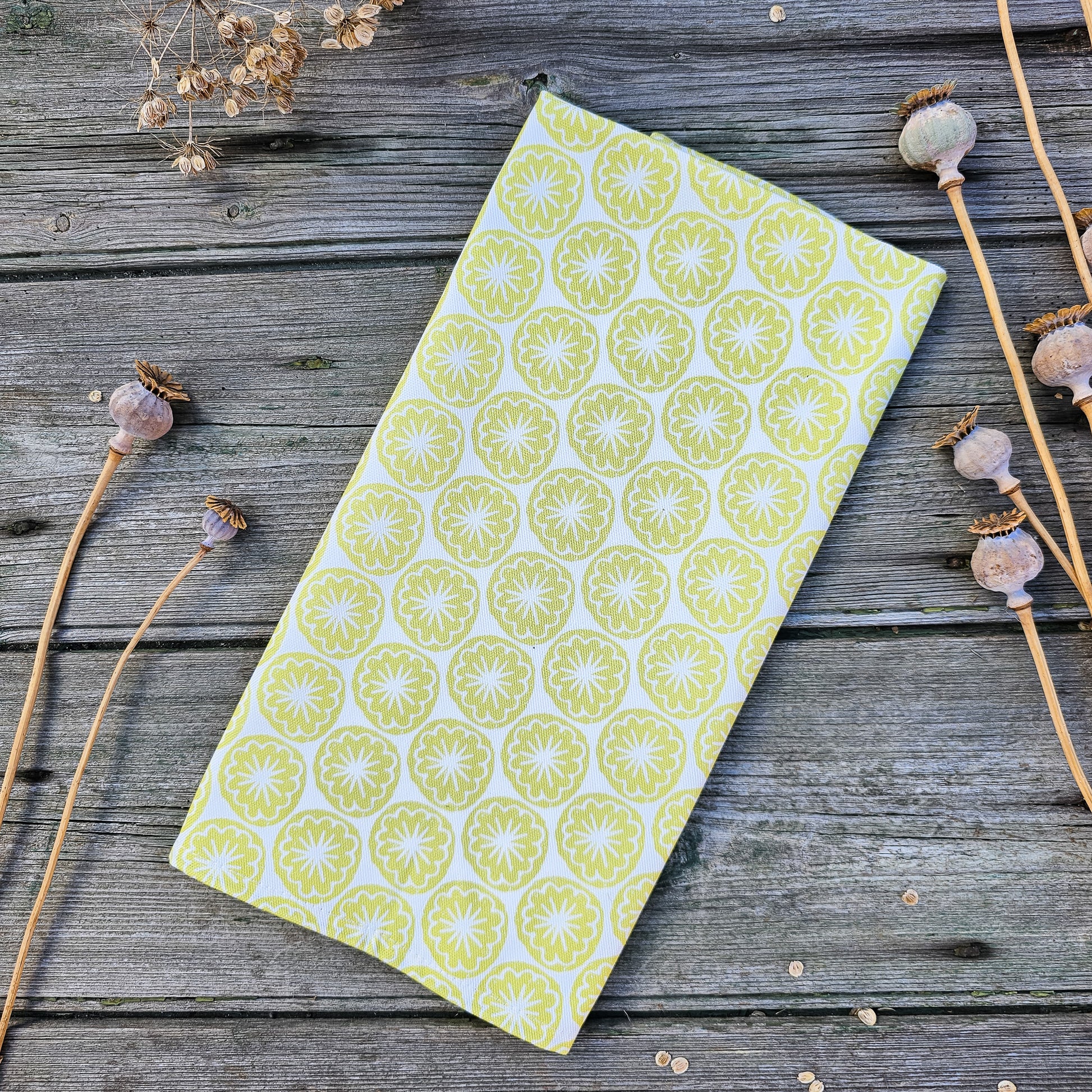 Yellow Seedhead patterned fabric folded on a wooden surface, featuring bold circular  yellow botanical motifs — ZIA LIVING