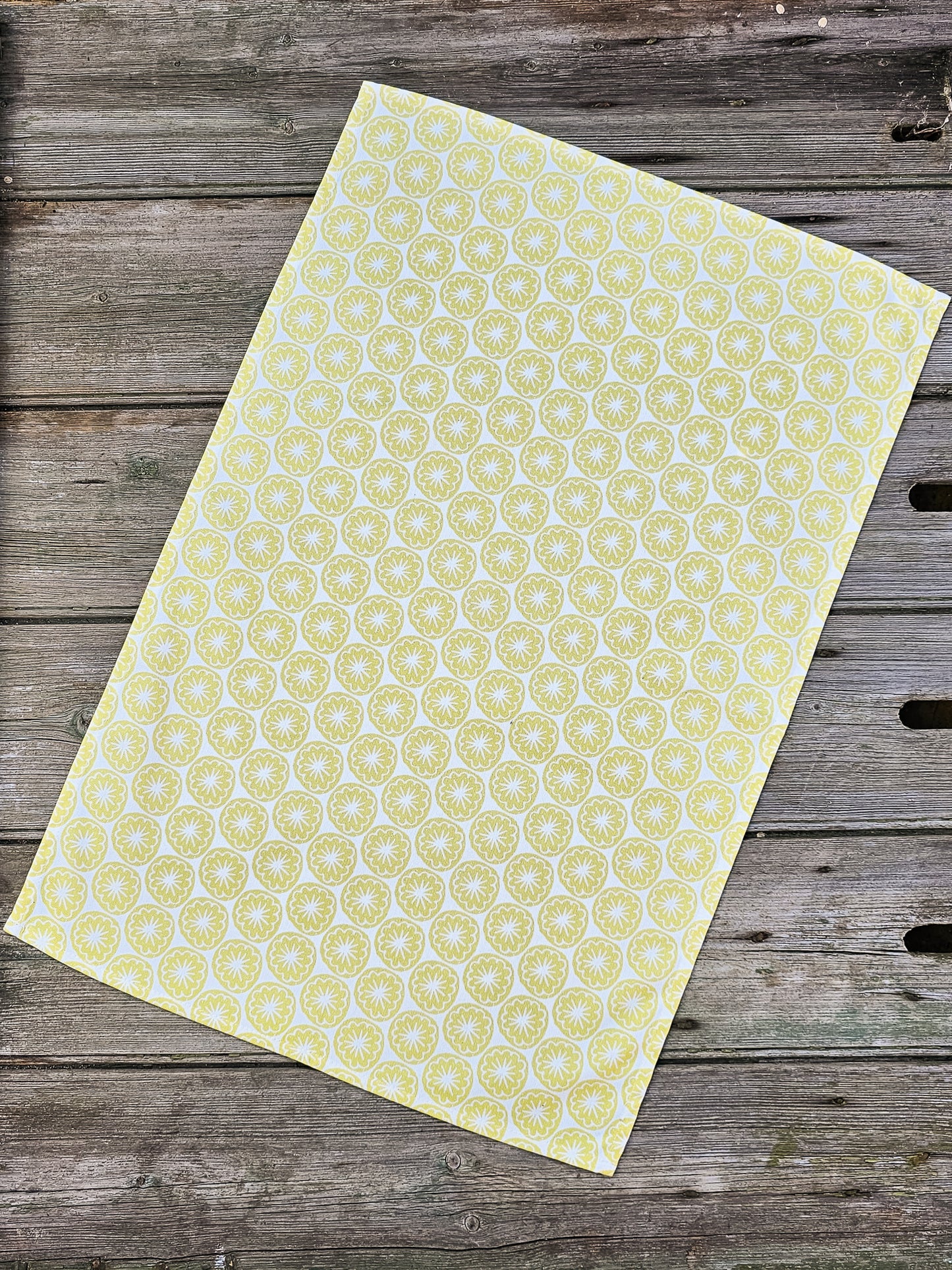 A yellow Poppy Seed Head tea towel  from ZIA LIVING showing full design on vintage wooden surface