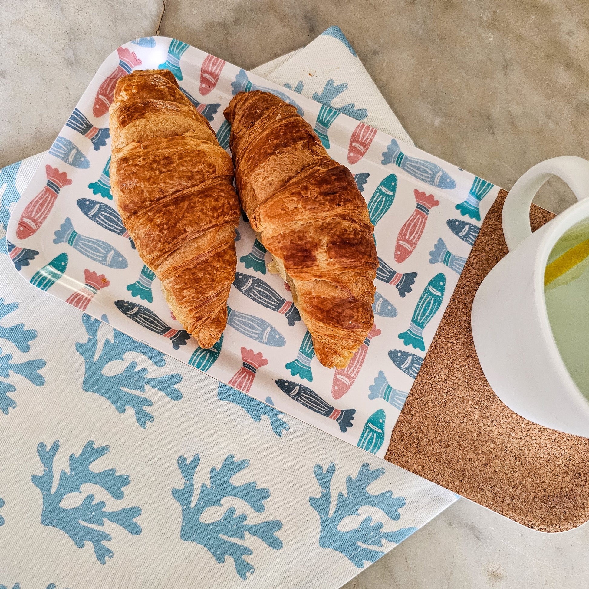 ZIA LIVING rectangular serving tray featuring a colourful fish pattern with a natural cork section, featured with seaweed tea towel and pastries.