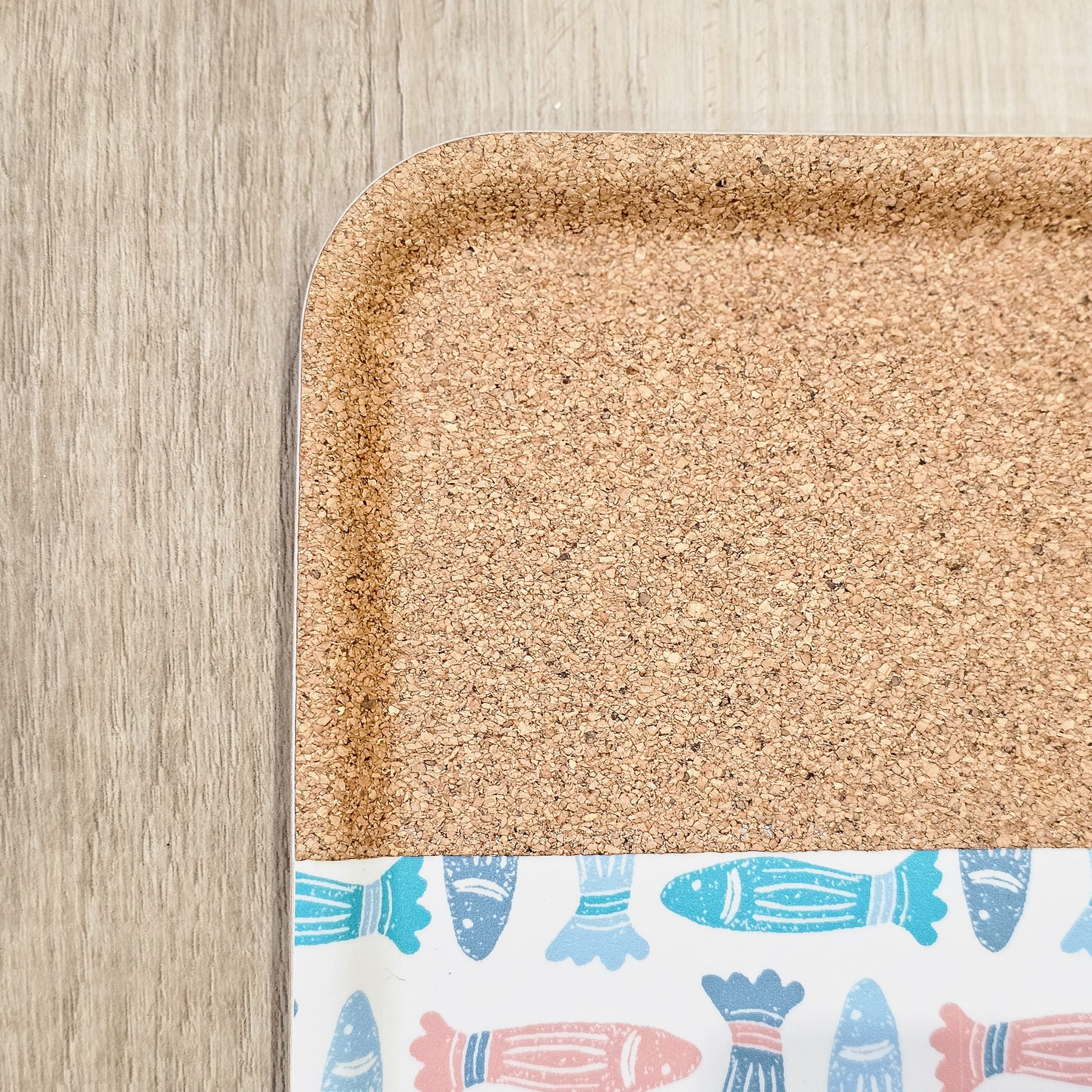 ZIA LIVING rectangular serving tray featuring a colourful fish pattern with a natural cork section, close up on wooden surface.