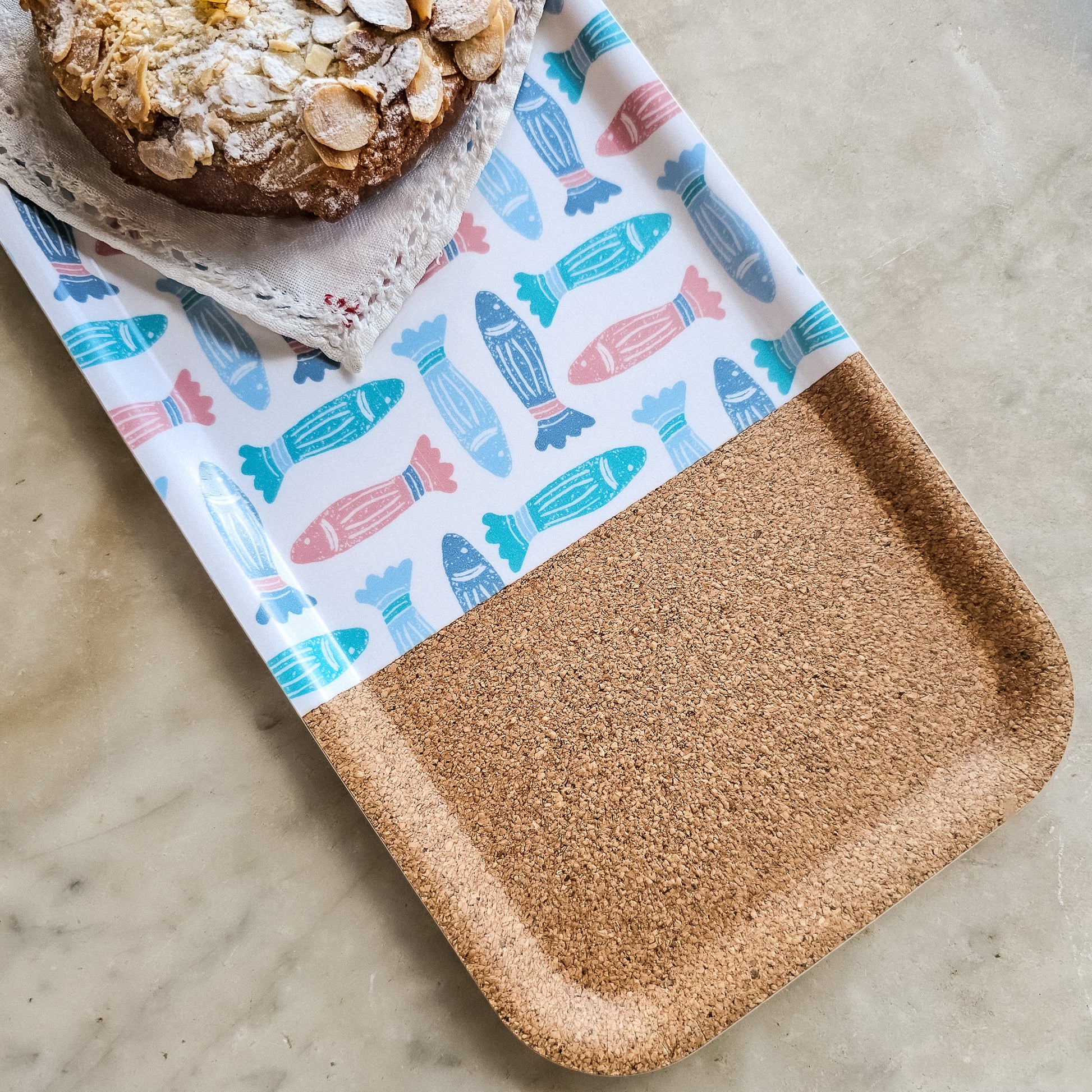 ZIA LIVING rectangular serving tray featuring a colourful fish pattern with a natural cork section, displayed on a marble worktop with pastry