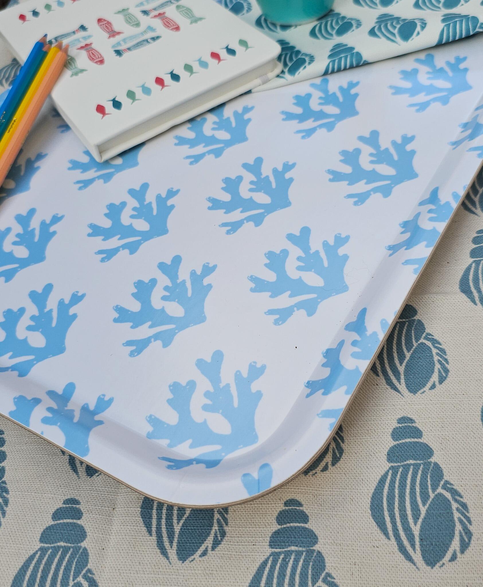 Zia Living sky blue serving tray with a geometric seaweed pattern, made from birch wood with a melamine surface, styled with coloured pencils, a coastal‑print notebook, on a seashell‑patterned fabric