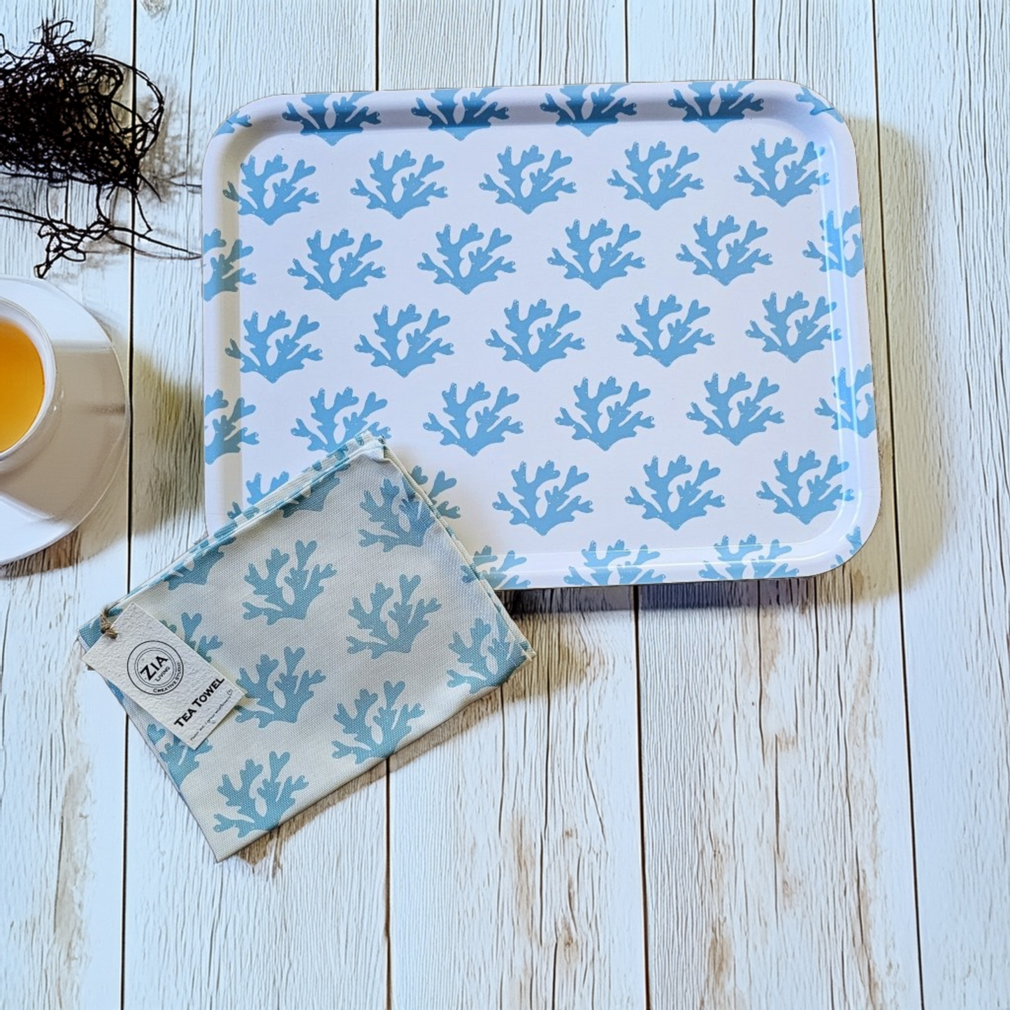 White rectangular tray with a soft blue seaweed coral pattern styled on a light wooden surface, paired with a matching blue‑coral tea towel and a cup of tea for a calm coastal flat‑lay. ZIA LIVING.