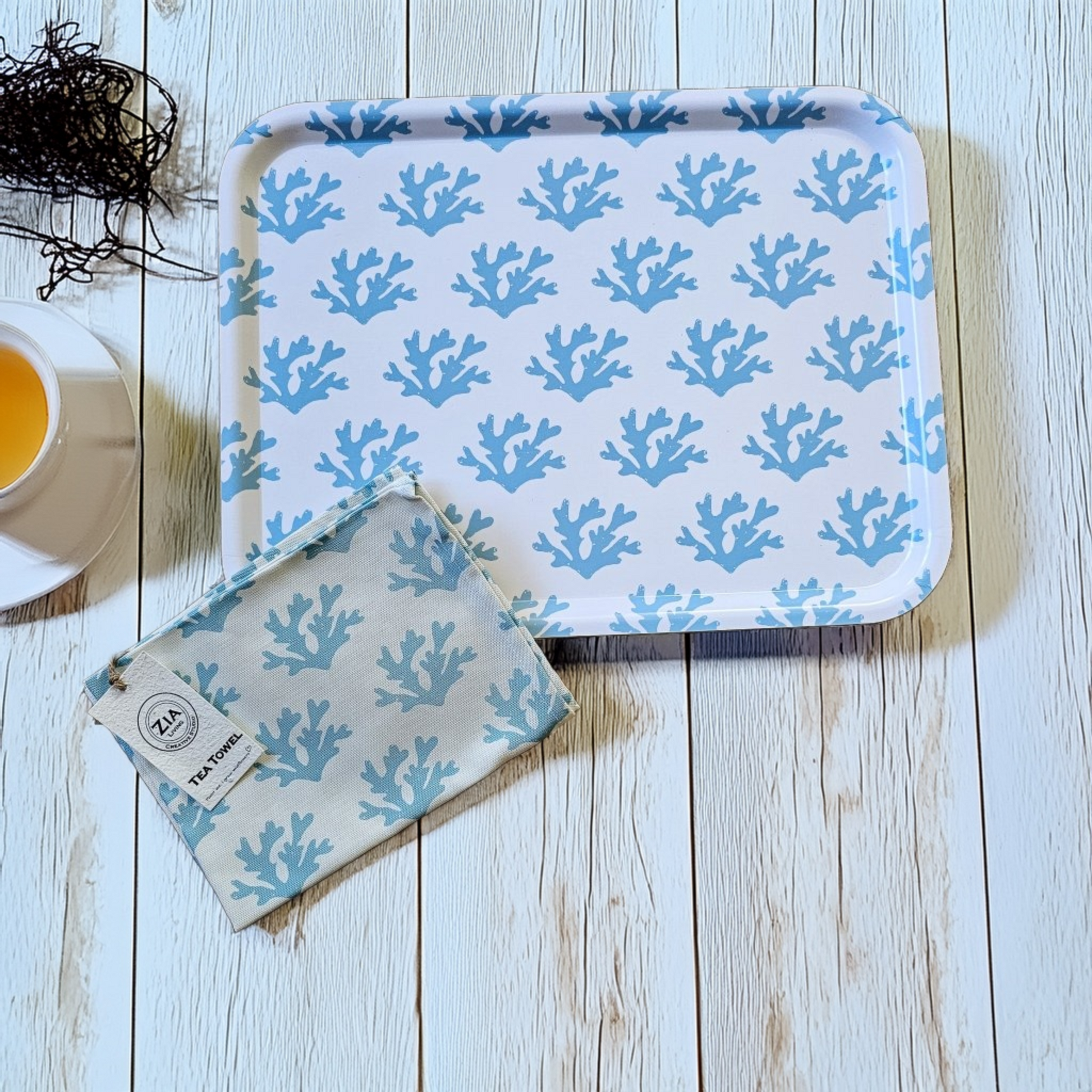 White rectangular tray with a soft blue seaweed coral pattern styled on a light wooden surface, paired with a matching blue‑coral tea towel and a cup of tea for a calm coastal flat‑lay. ZIA LIVING.